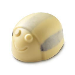 A shiny, pale yellow LUSH Humbug Scrubee solid body scrub is shown against a light gray background. The product is shaped like a bee with an engraved smiling face and stripes on its back.