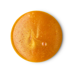 A smooth, glossy, circular puddle of LUSH Golden Pear shower gel is shown against a light gray background. The shimmering golden-orange product has a few small air bubbles in it.