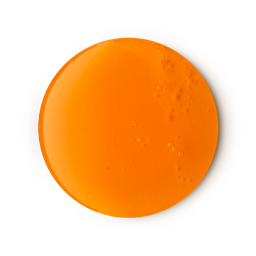 A smooth, glossy, circular puddle of LUSH Merry Christmas Everyone shower gel is shown against a light gray background. The vibrant orange product has a few small air bubbles in it.