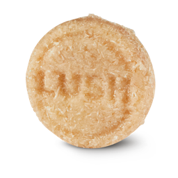 Honey I Washed My Hair. A round, textured, pale beige Lush solid shampoo bar. The bar has a rough, shredded-coconut texture and is embossed with the "LUSH" logo in the centre.