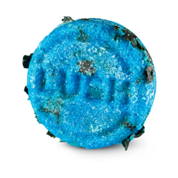 Seanik. A circular, bright blue Lush solid shampoo bar embossed with the word 'LUSH' in the centre. The highly textured bar is speckled with pieces of dark green seaweed.