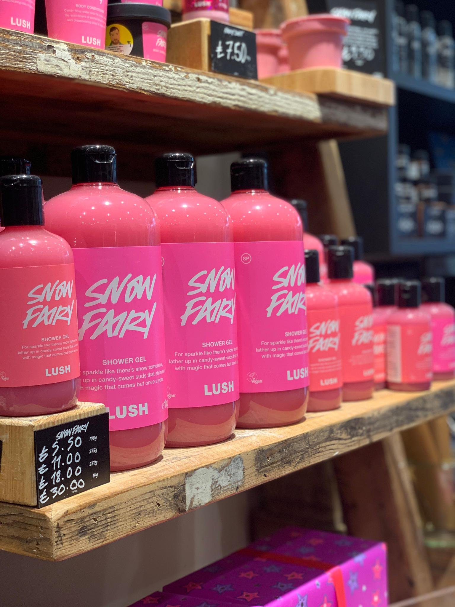 Bottles of pink Snow Fairy shower gel on a wooden shelf.