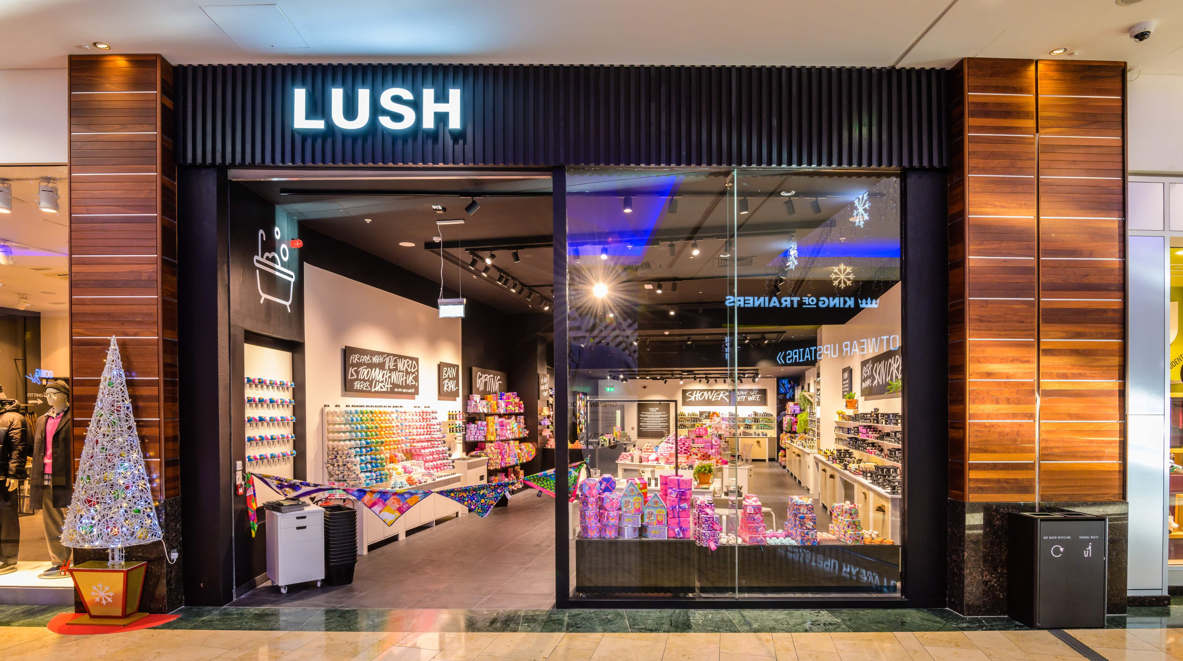 Exterior view of the shop. Large open door with illuminated Lush sign above. Large glass window allowing full view of the interior of the shop.