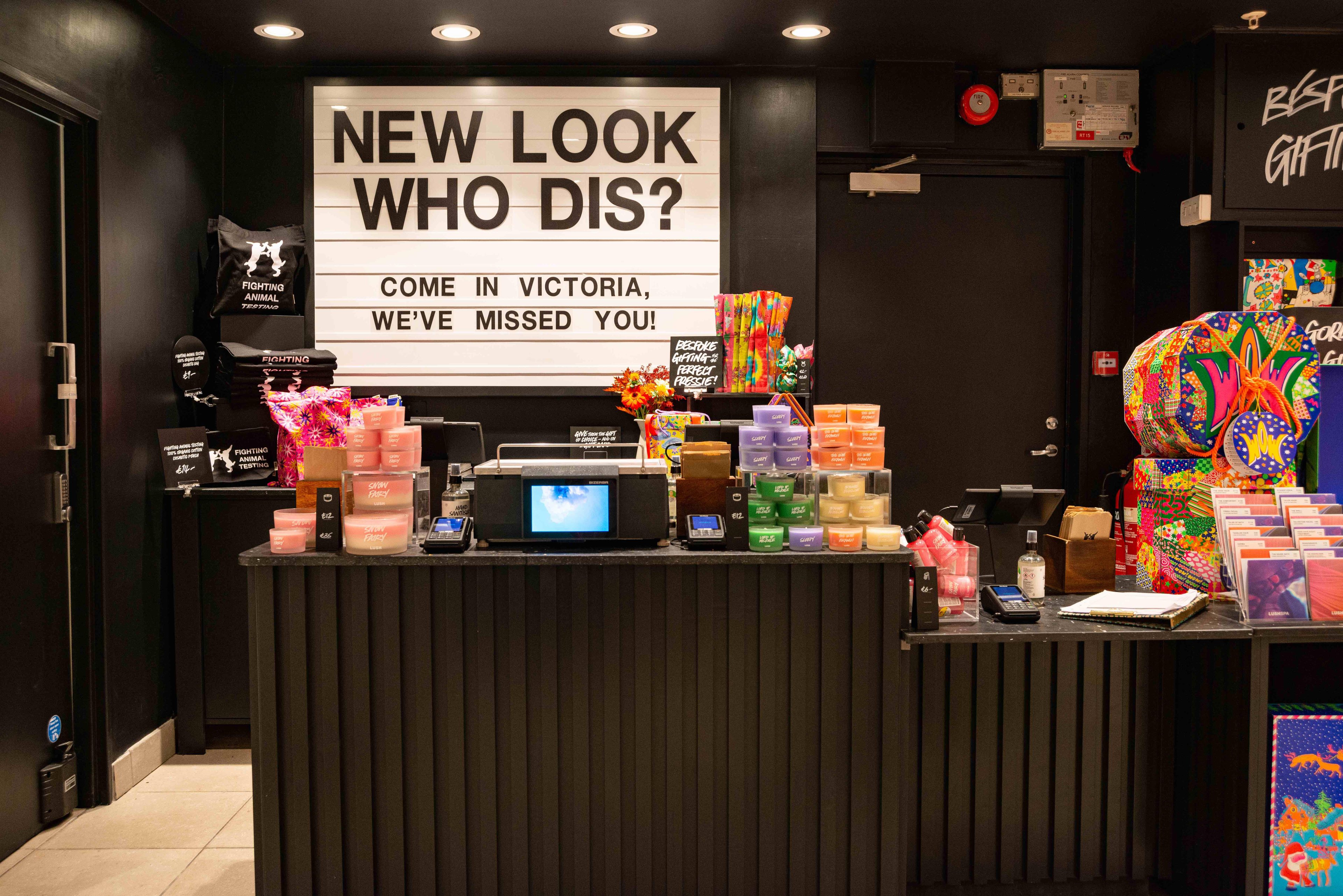 Interior view. Till point with products displayed on top of it. Cinema style display board behind reads New Look Who Dis? Come In Victoria We've Missed You.