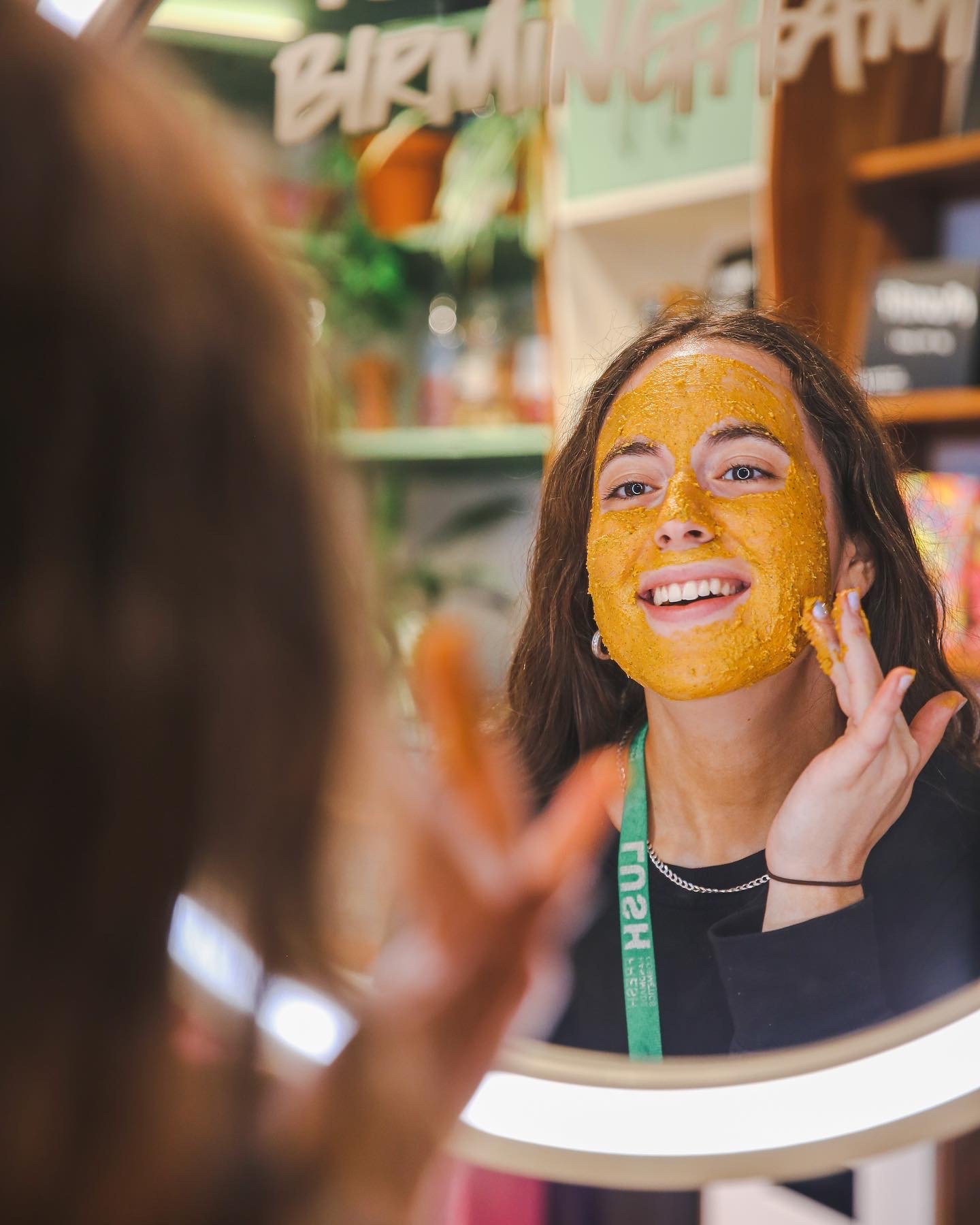 Member of staff applying a fresh face mask whilst looking in the mirror and smiling.