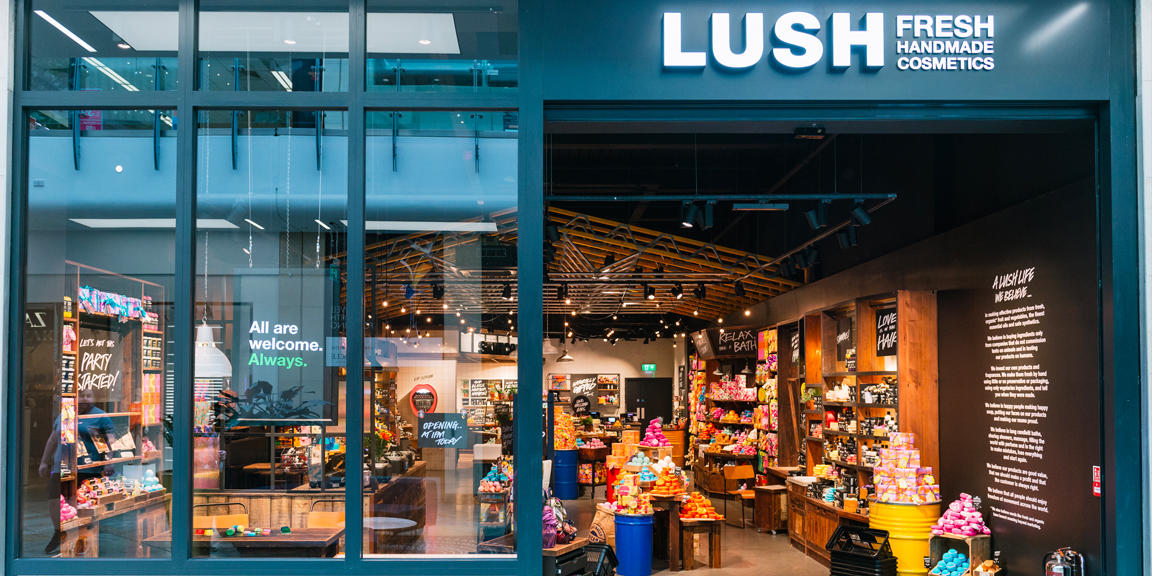 Reading shop front. Exterior view of shop. Black framed shop with glass frontage. Large entrance on the right with illuminated Lush sign above. Products displayed in window to left of entrance.