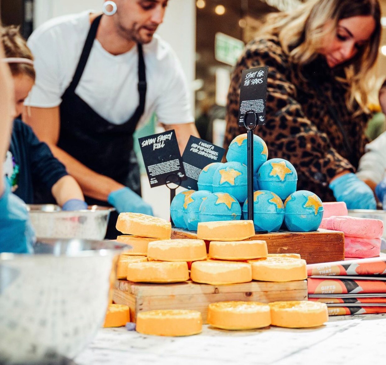 In the foreground are mounds of unpackaged products. In the background are members of staff making products.