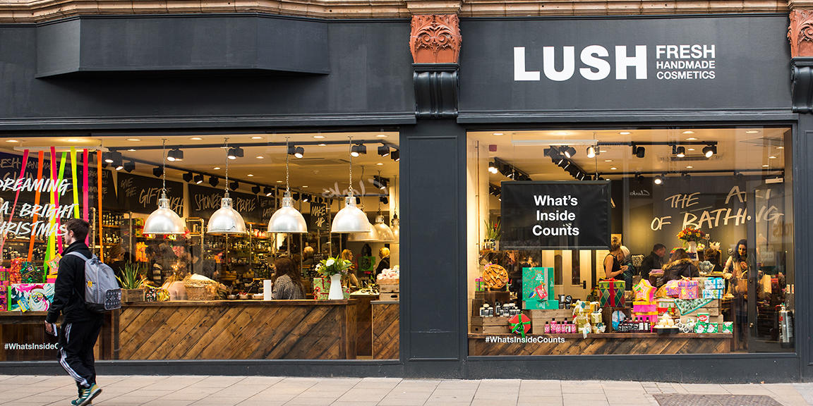 Leeds shop front. Exterior view of shop. Black framed shop with glass frontage. Large Lush sign above the right hand side window. Large displays of product visible in both windows, the right hand window has a sign that reads What's Inside Counts.