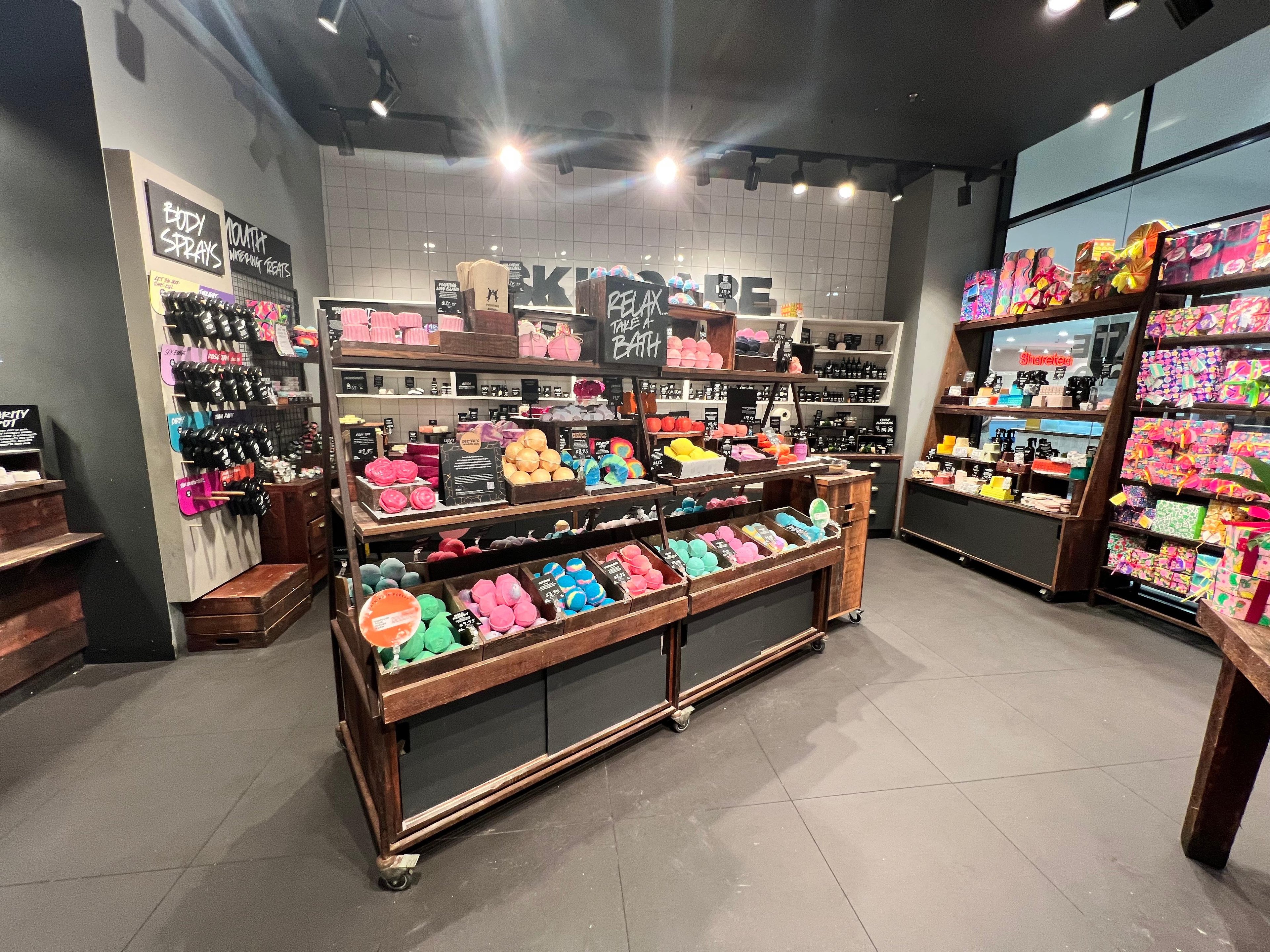 Interior view of shop, foreground has a display of unpackaged bath products of various sizes and colours in a wooden and metal display unit.