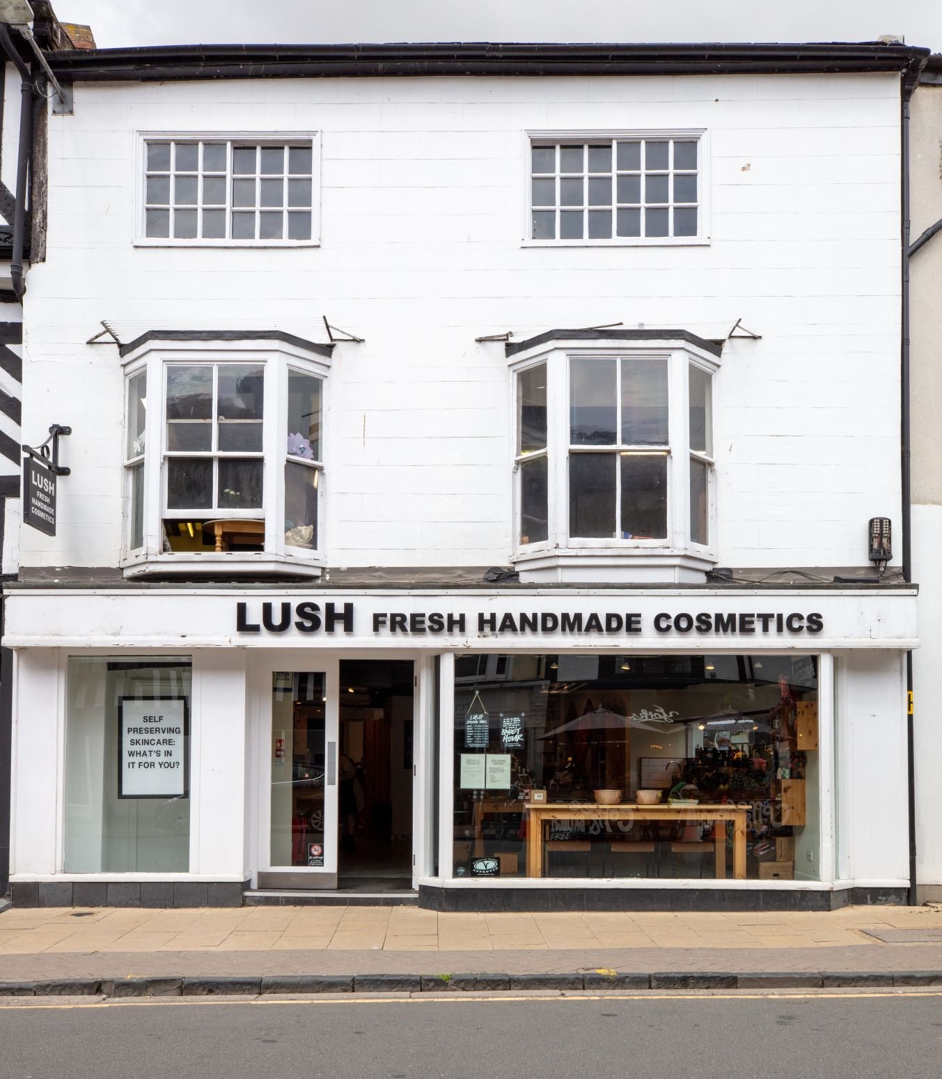Stratford upon Avon Store. Exterior view of shop. White and black shopfront with large glass window. Entrance in centre with  Lush sign above. Products displayed in window to the right side of entrance.