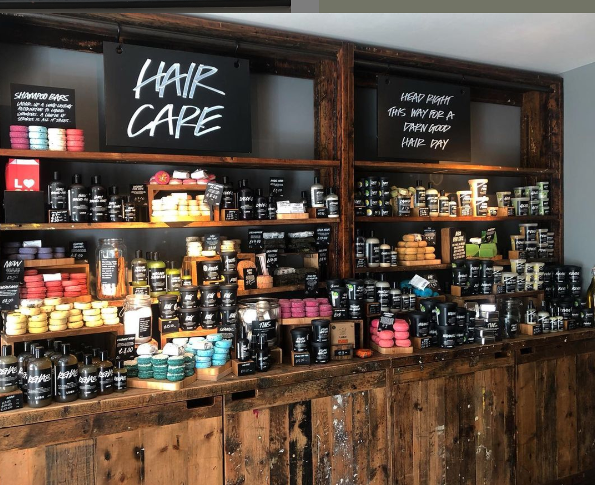 Interior view of shop. Various packaged and unpackaged haircare products displayed on countertop and wooden shelves above. Signs read Hair Care and Head Right This Way For A Darn Good Hair Day