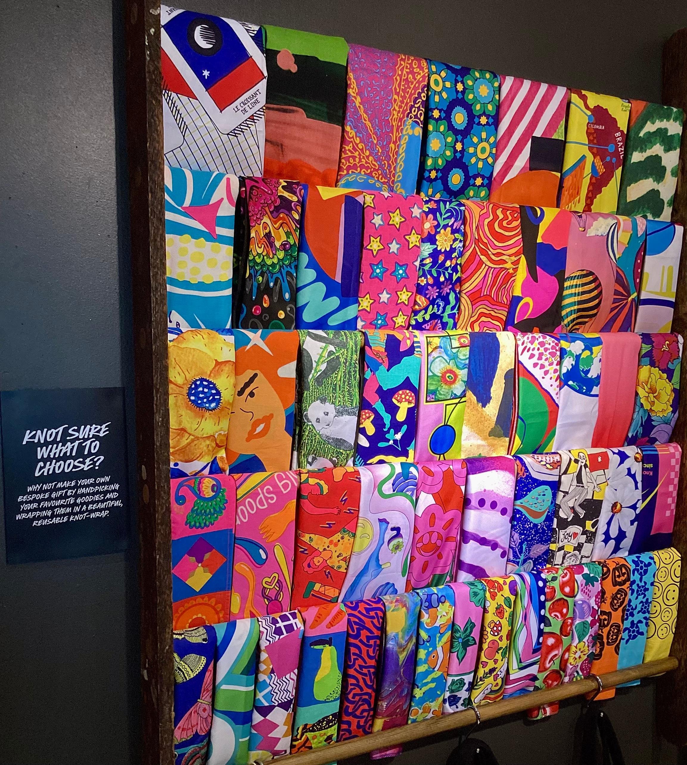 Interior view of shop. Large brightly coloured display of various knotwrap scarves.