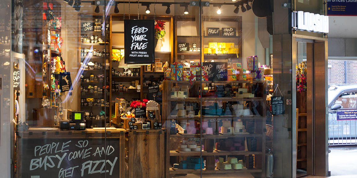 Waterloo shop front. Exterior view of shop. Glass fronted shop. Entrance to the right with illuminated Lush sign above. Products displayed in windows along full length of shop.