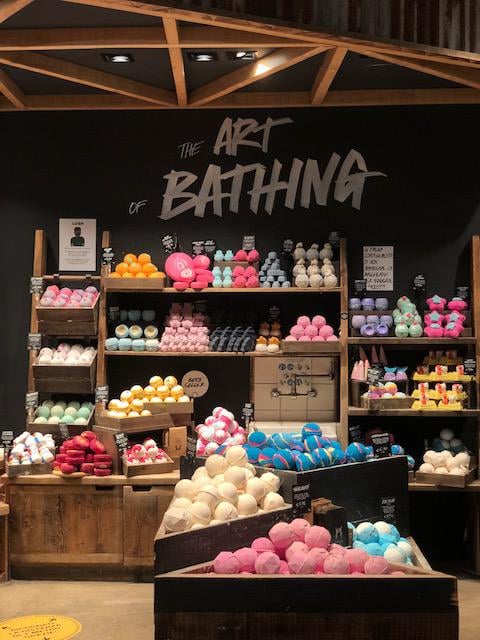 Large display of unpackaged brightly coloured bath products creating mounds of colour. Sign above reads The Art Of Bathing
