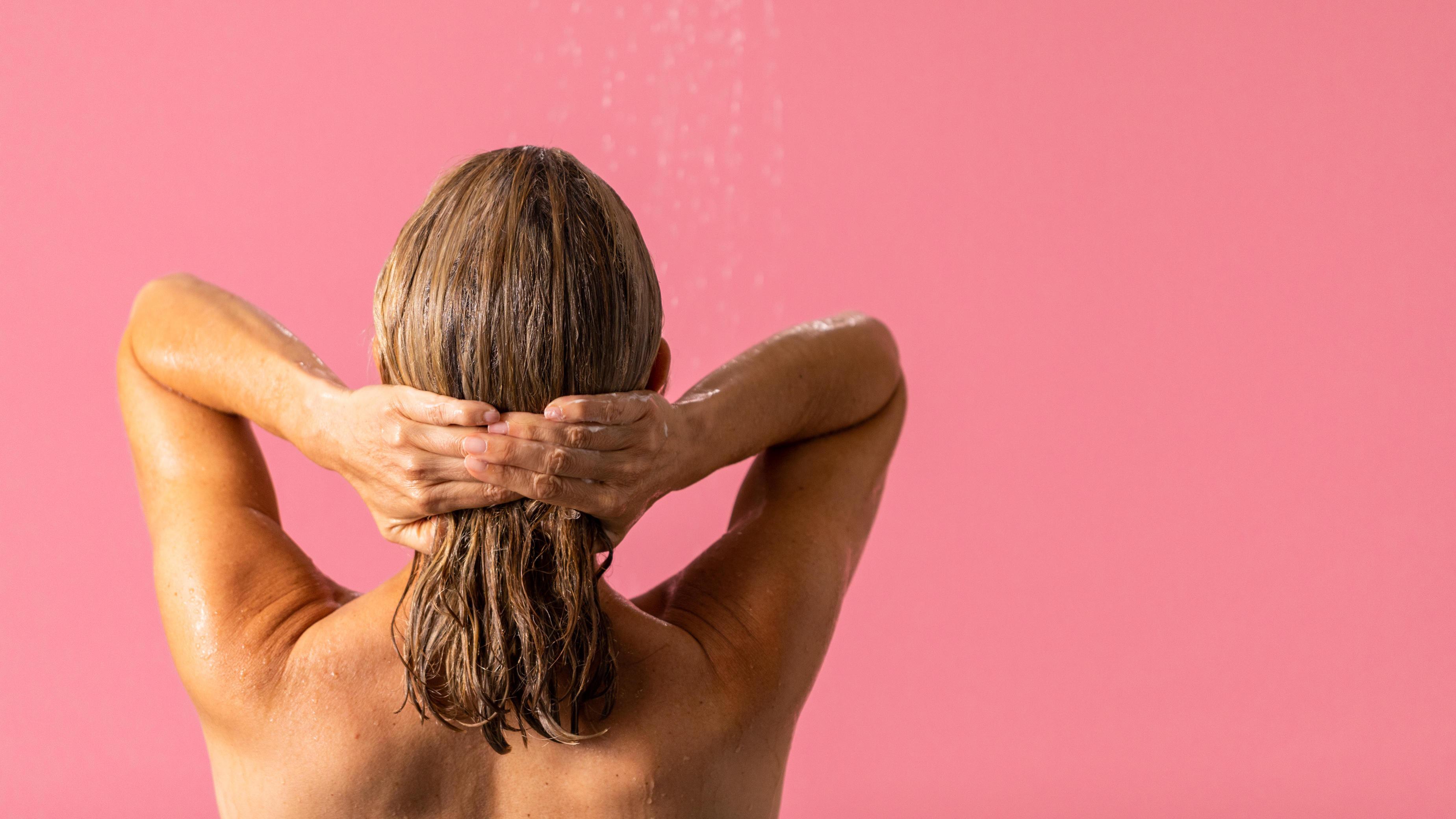 Person with medium length hair facing away from the camera. They are holding their hair back with both hands.