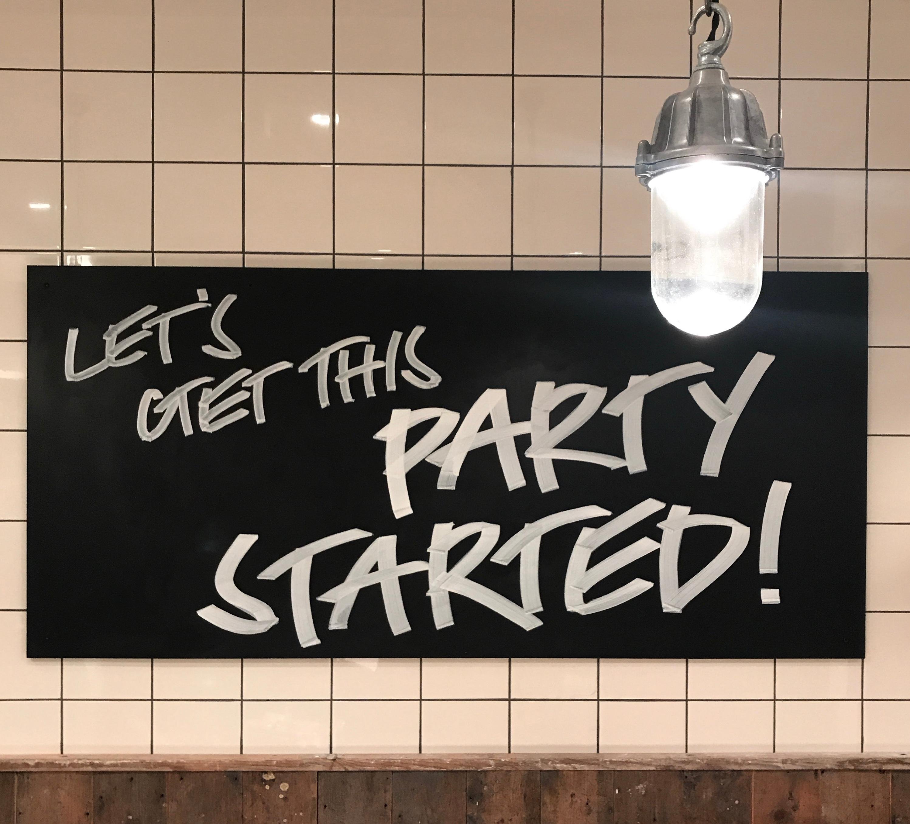 White tiled wall with black sign that reads Lets Get This Party Started!