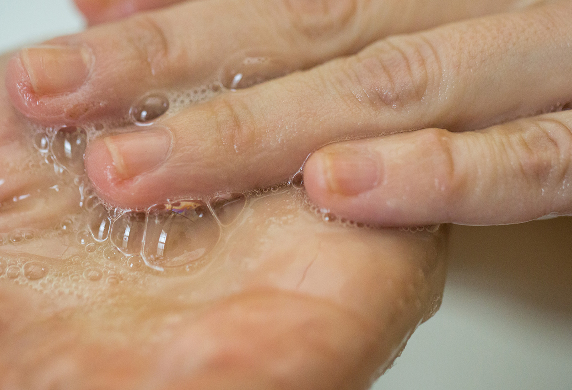 A pale yellow, almost clear, shampoo is rubbed into the palm of the hand, creating lots of bubbles.
