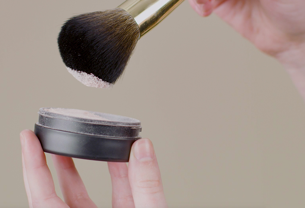 People Powder, a large, dome-shaped powder brush, picks up fine, light pink powder from a pot of Emotional Brilliance.
