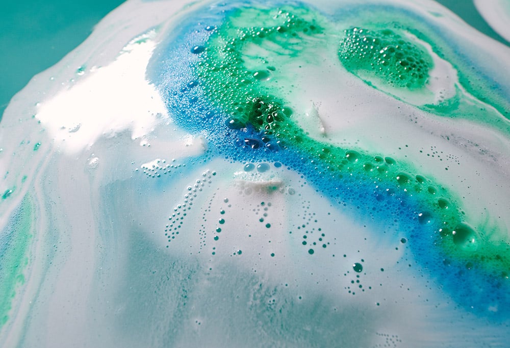 Swirls of white, blue and green fizz from Happy Face bath bomb.