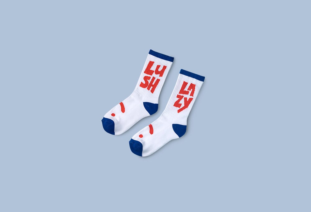 White, navy blue and red socks with happy face design on them and Lush and Lazy on them.
