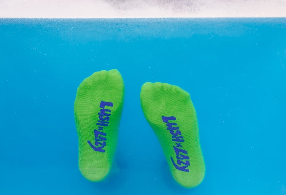 Green and navy blue socks, bottom view with the Lush x Lazy logo on them.
