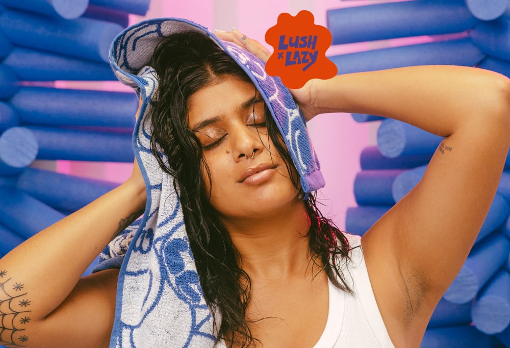 A model uses the hand towel on their hair with purple foam swimming floats behind them and a pink background.