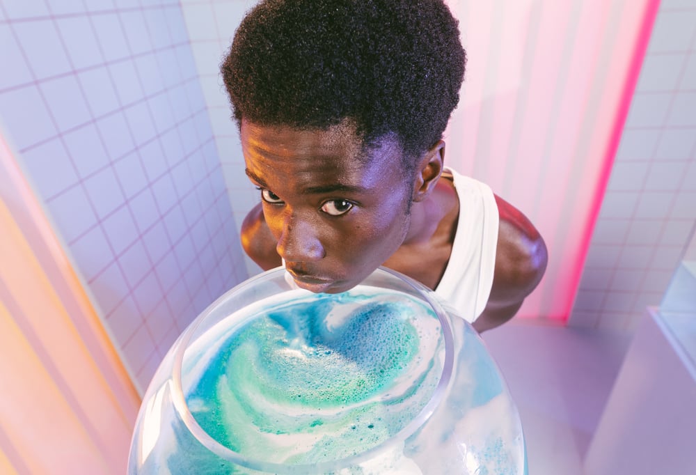 a Model holds a large glass sphere full of green, blue and white Sad Face bath bomb water