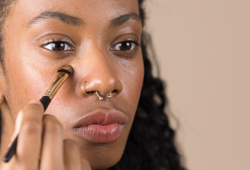 A person appears focused, as they get To The Point, a small concealer brush, working with concealer in the under eye area.