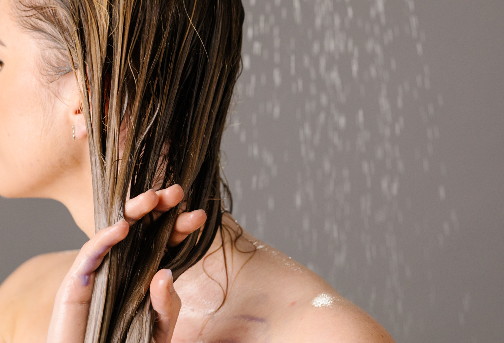 A person works their fingers through their long, wet, blonde hair while using Aga's lilac hair conditioner.