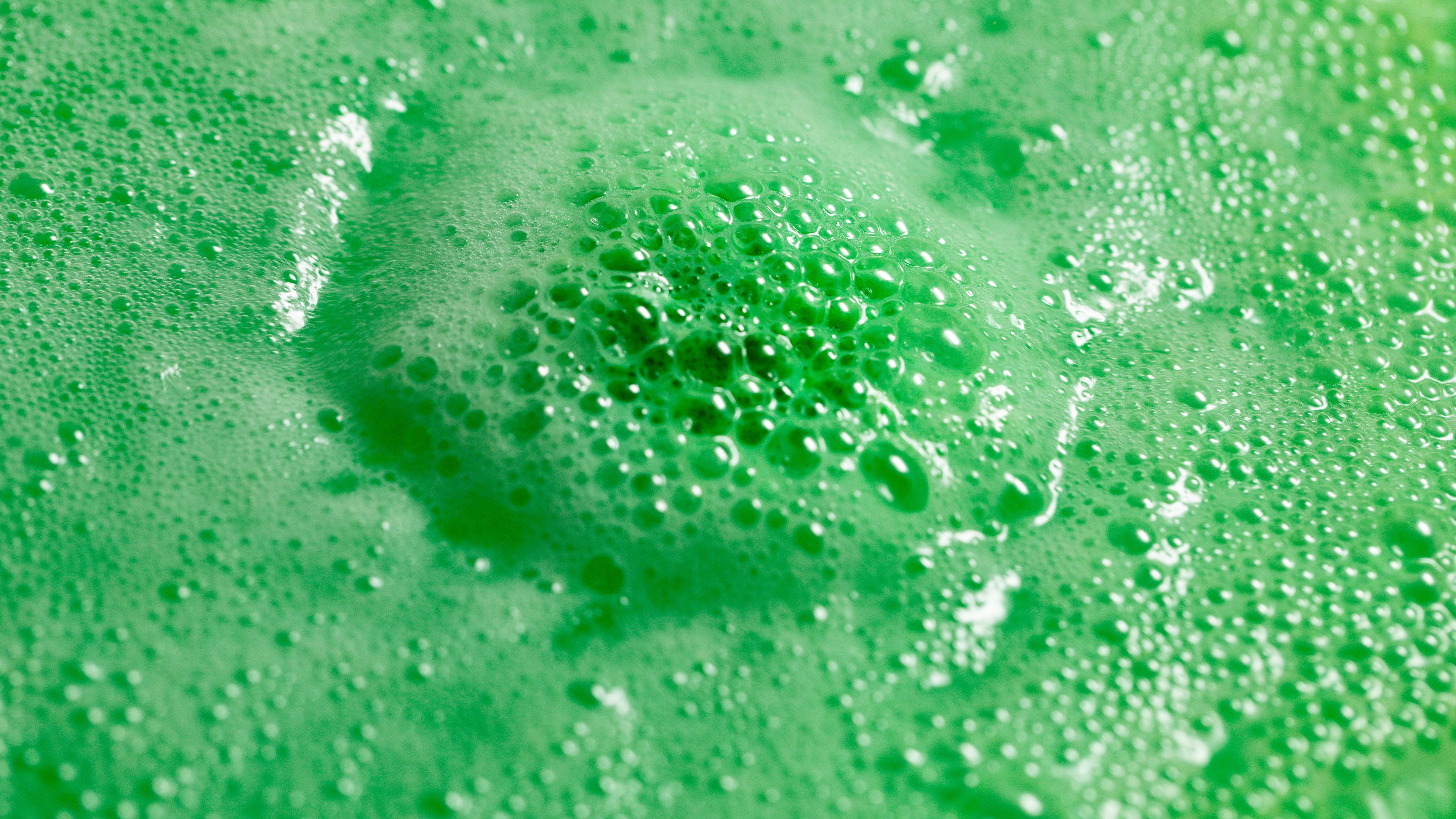 Avobath, a round lime green bath bomb, floating in aquamarine green water, encircled by a bubbly foam of the same colour.