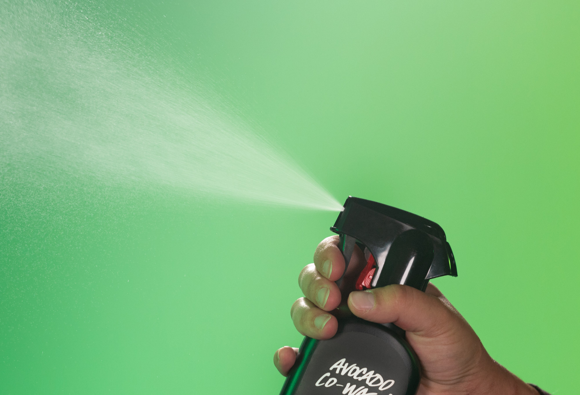 Avocado Co-Wash body spray is sprayed up into the air, in front of a vibrant light green background.