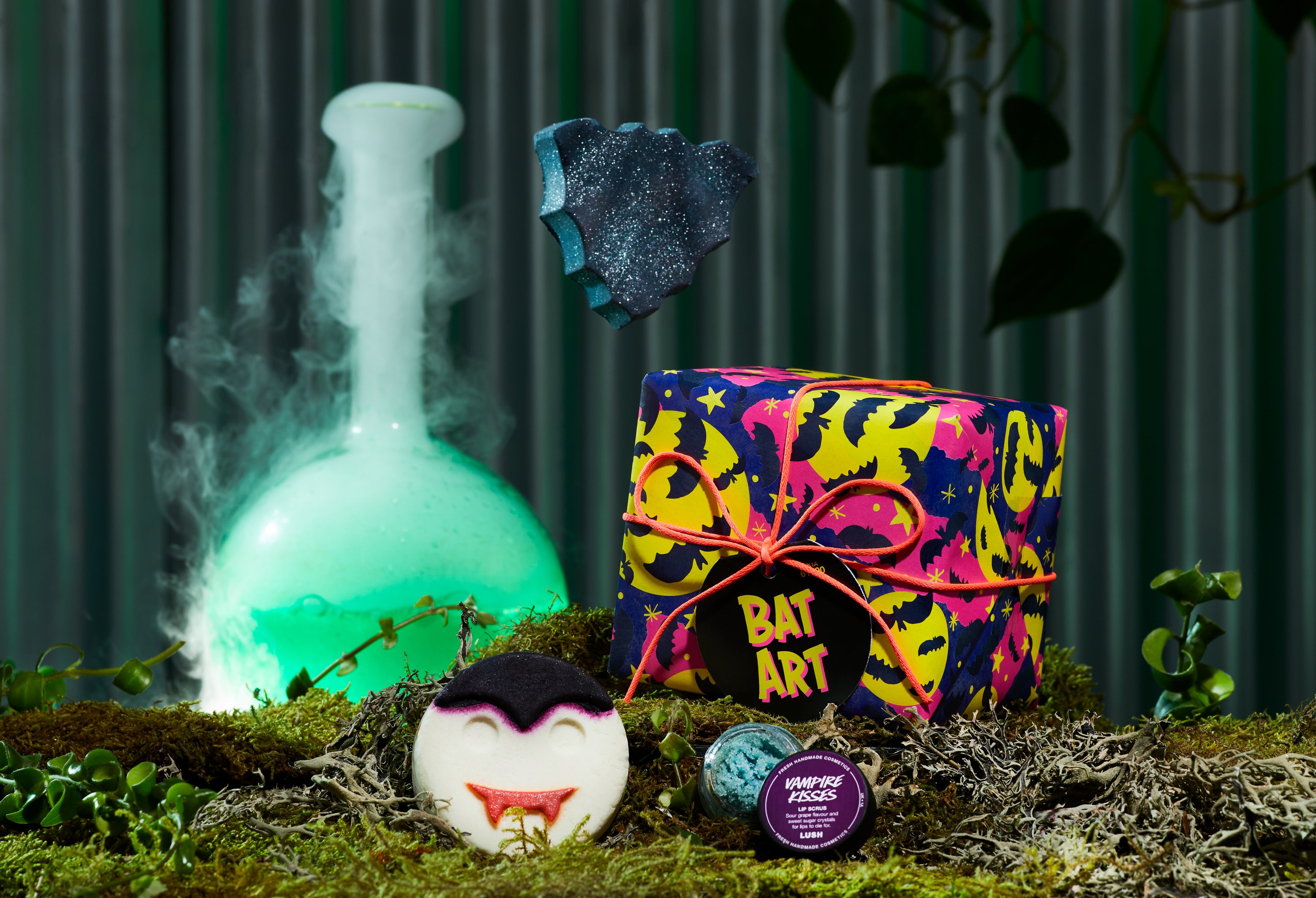 Bat Art gift, in front of a dark green background, surrounded by its products on a bed of moss. 