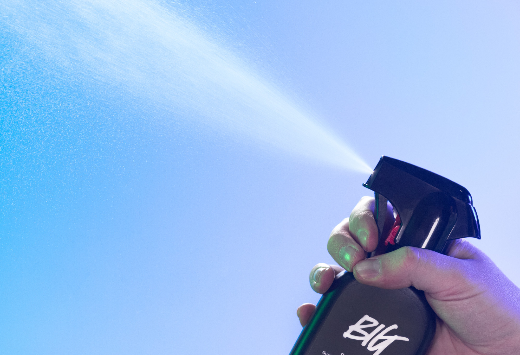Big body spray is sprayed up into the air, in front of a vibrant light blue background.