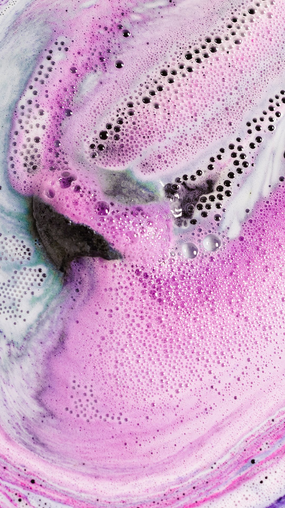 Black Rose bath bomb is buoyant, surrounded by a white, lilac and dark purple foam which is coming out like rays from the sun.