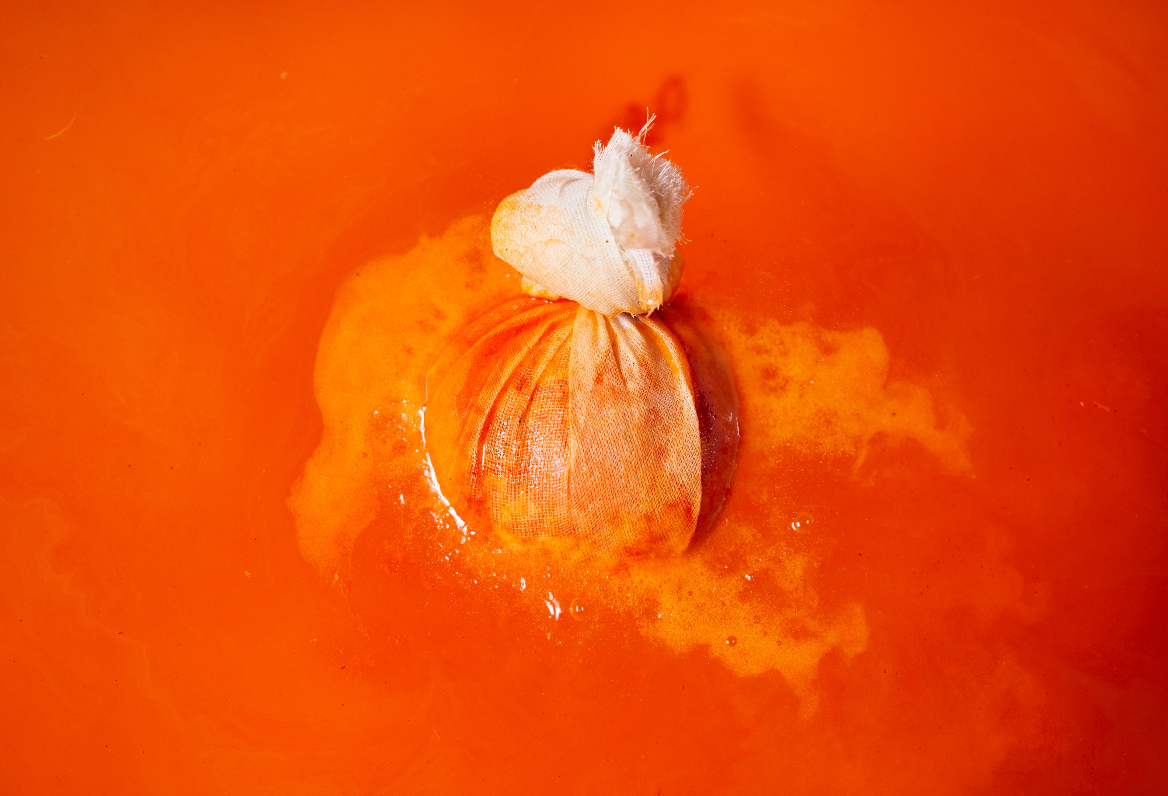 The bath bomb fizzes inside the muslin cloth, floating in deep orange coloured bath water.