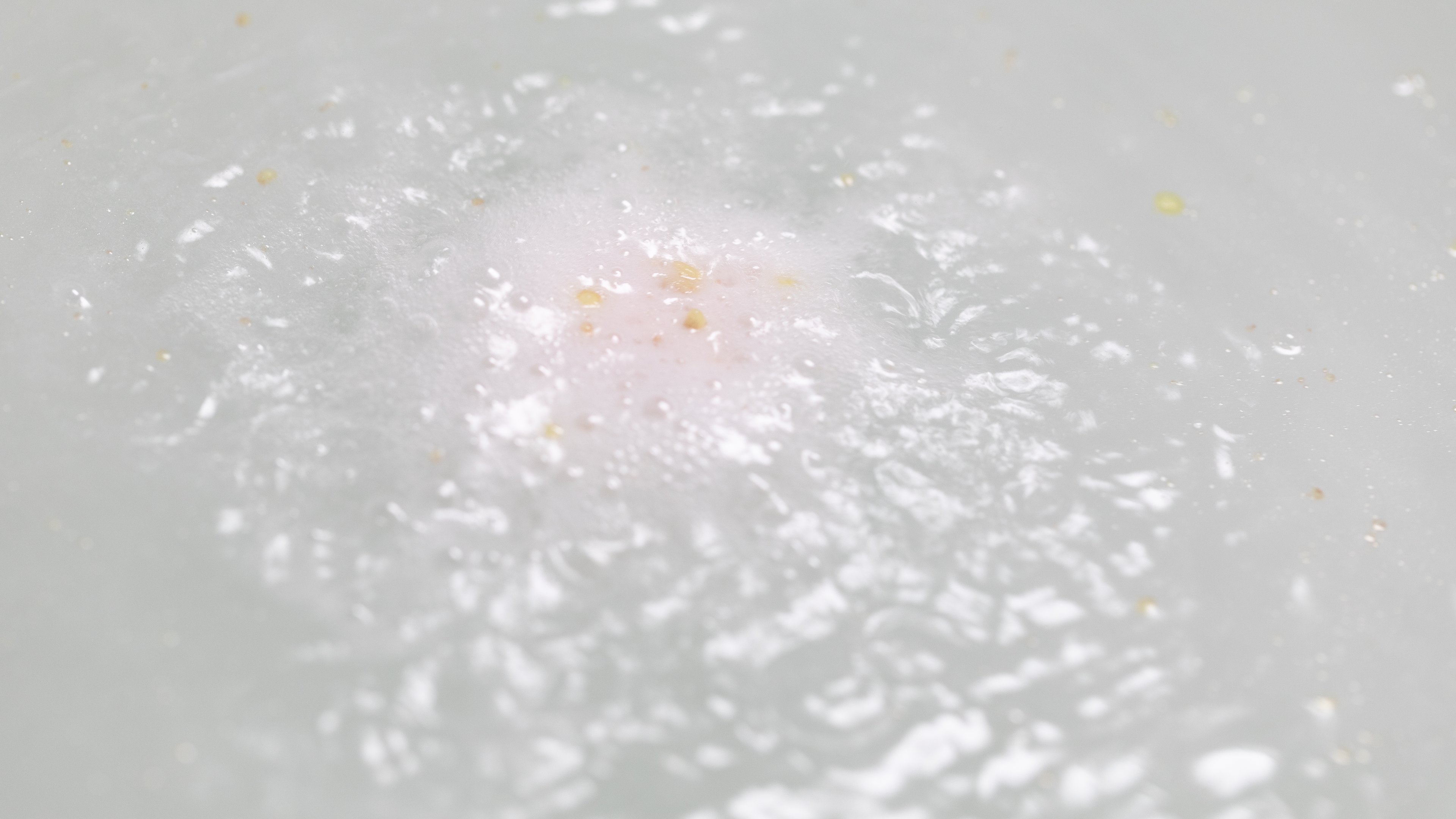 Butterball bath bomb in action, breaking down to reveal pieces of cocoa butter which float in the milky water it has created.