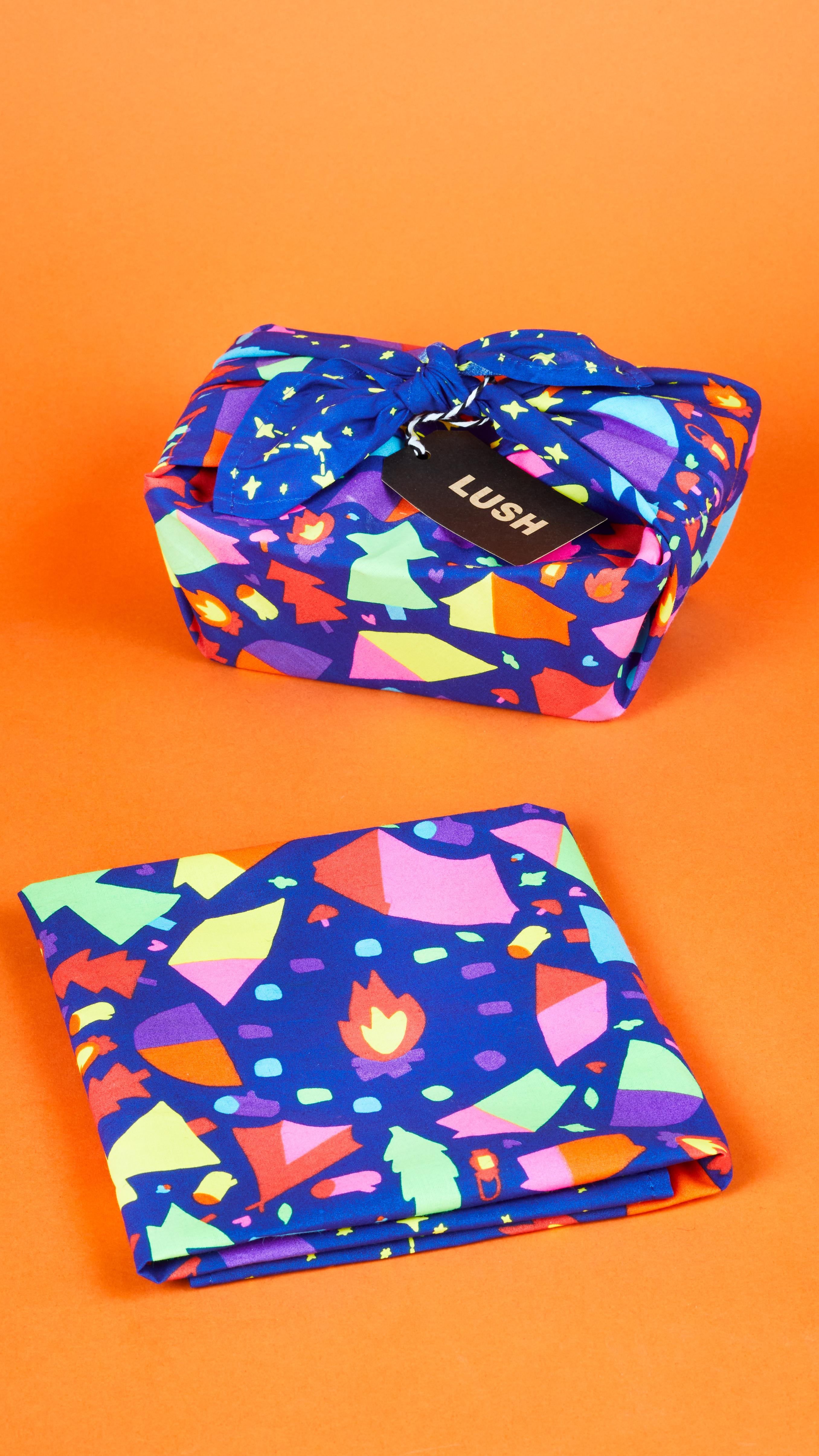 By The Campfire Knot Wrap displayed two different ways, folded and holding a gift, in front of a bright orange background.