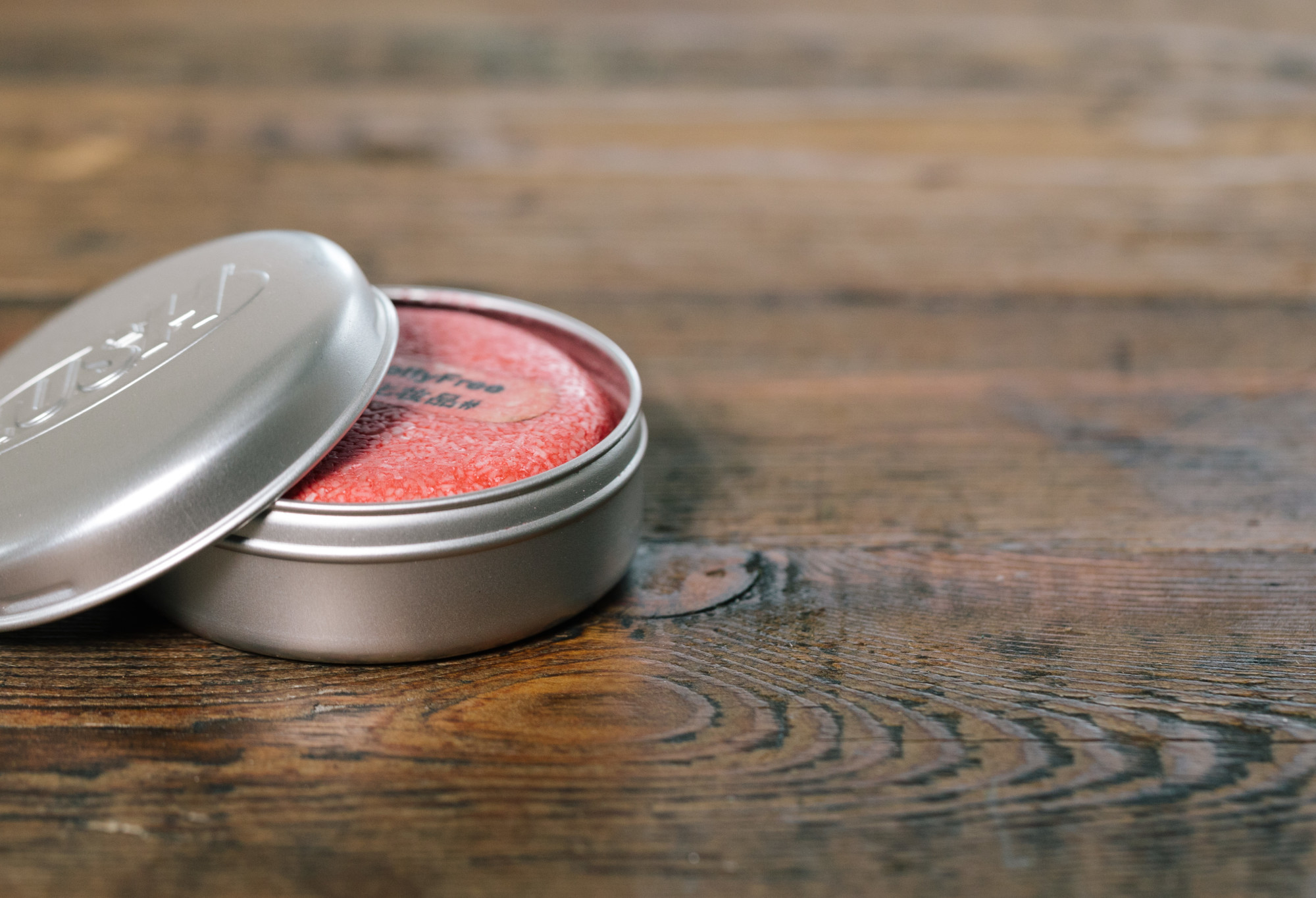 A round, silver metal product holder is being used to store a bright red New shampoo bar, just visible under the lid.