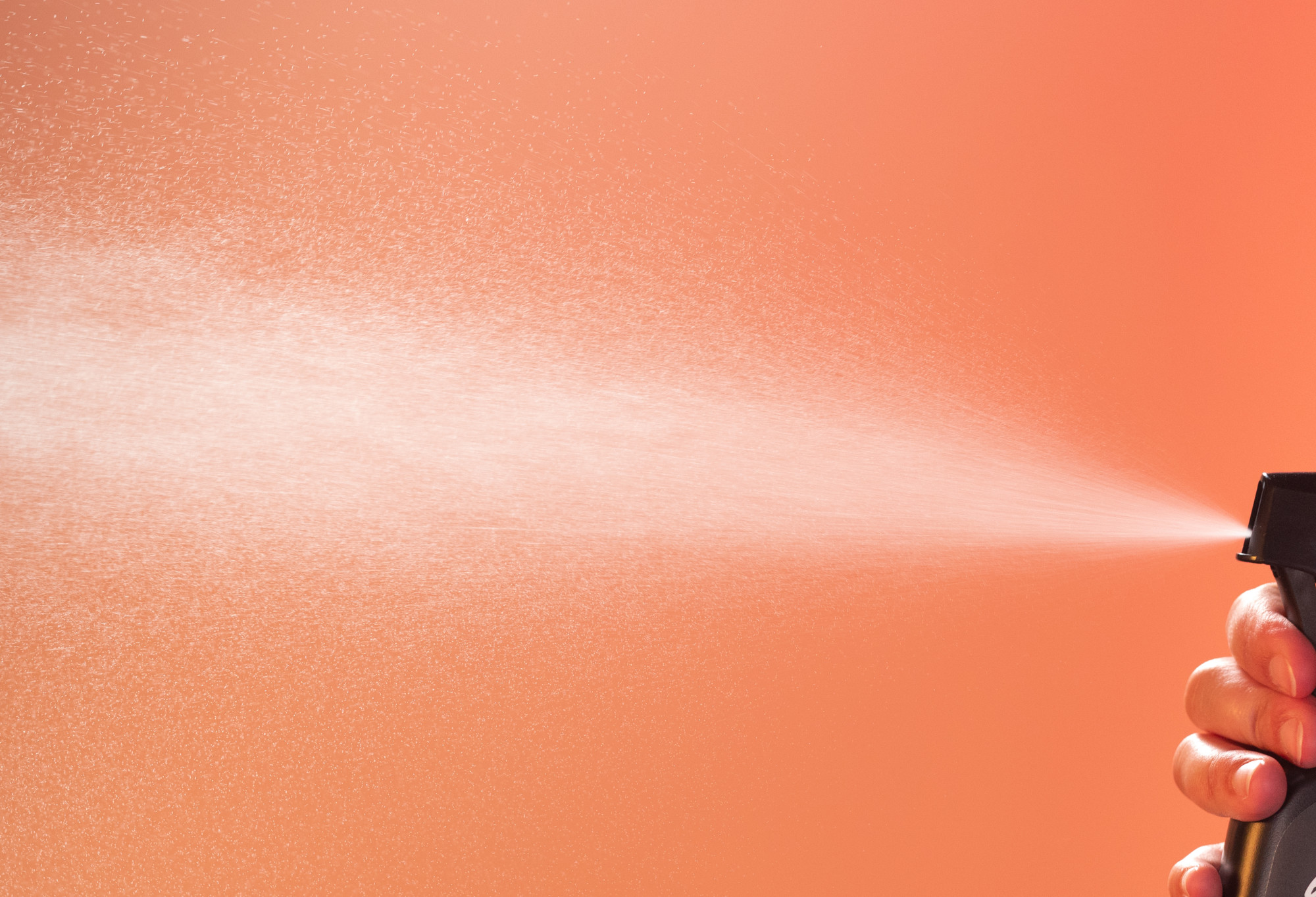 A huge spray of body spray shoots across a vibrant, deep orange background.