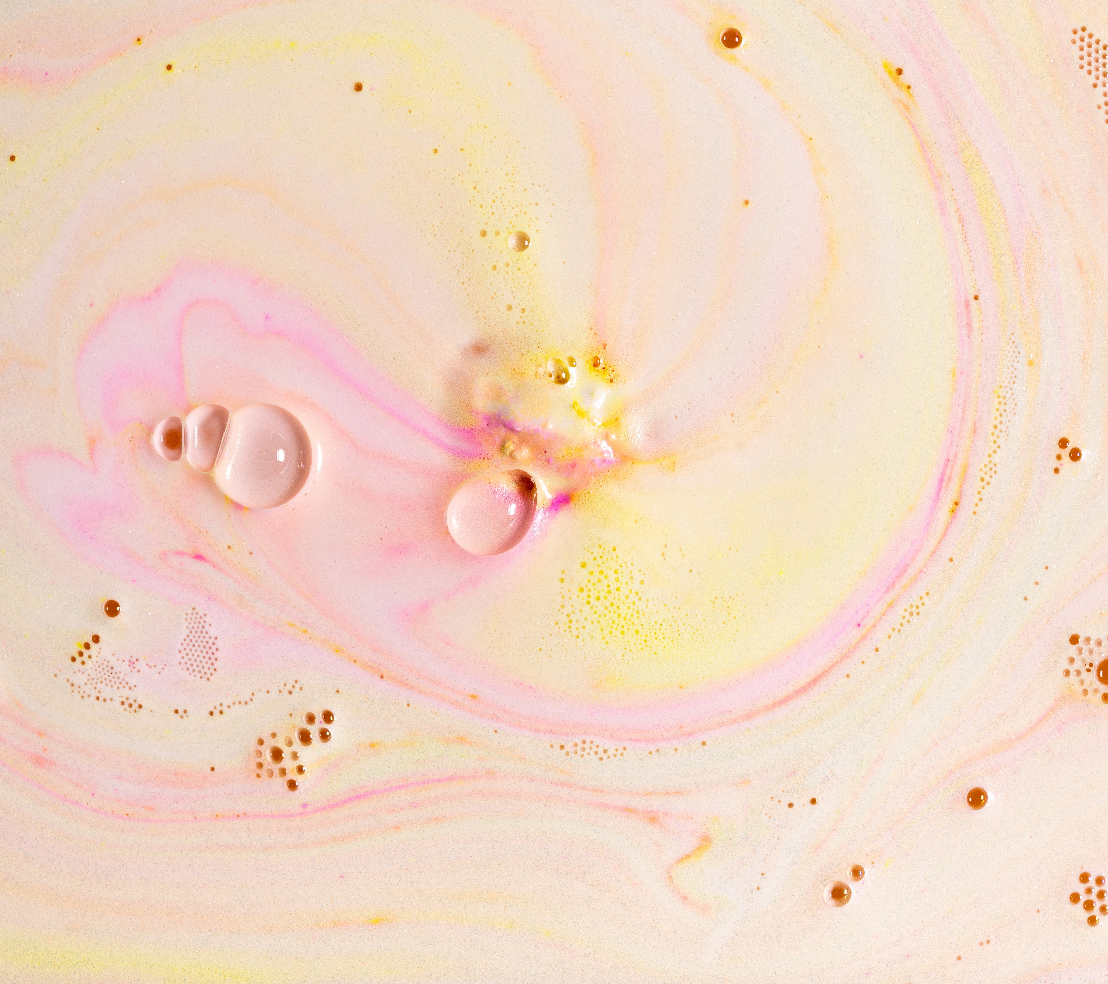Creamy yellow and pink swirls with hints of orange are created by a fizzing bath bomb, along with a variety of sizes of bubbles.