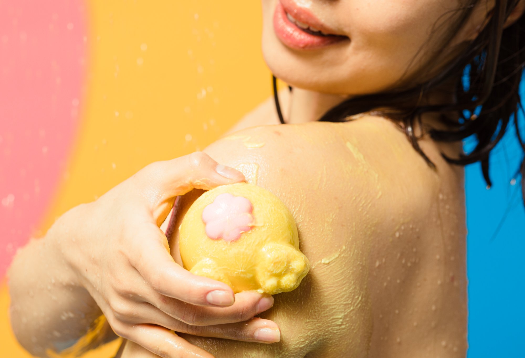 A model massages the body scrub over their shoulder, creating a creamy pale yellow lather. 