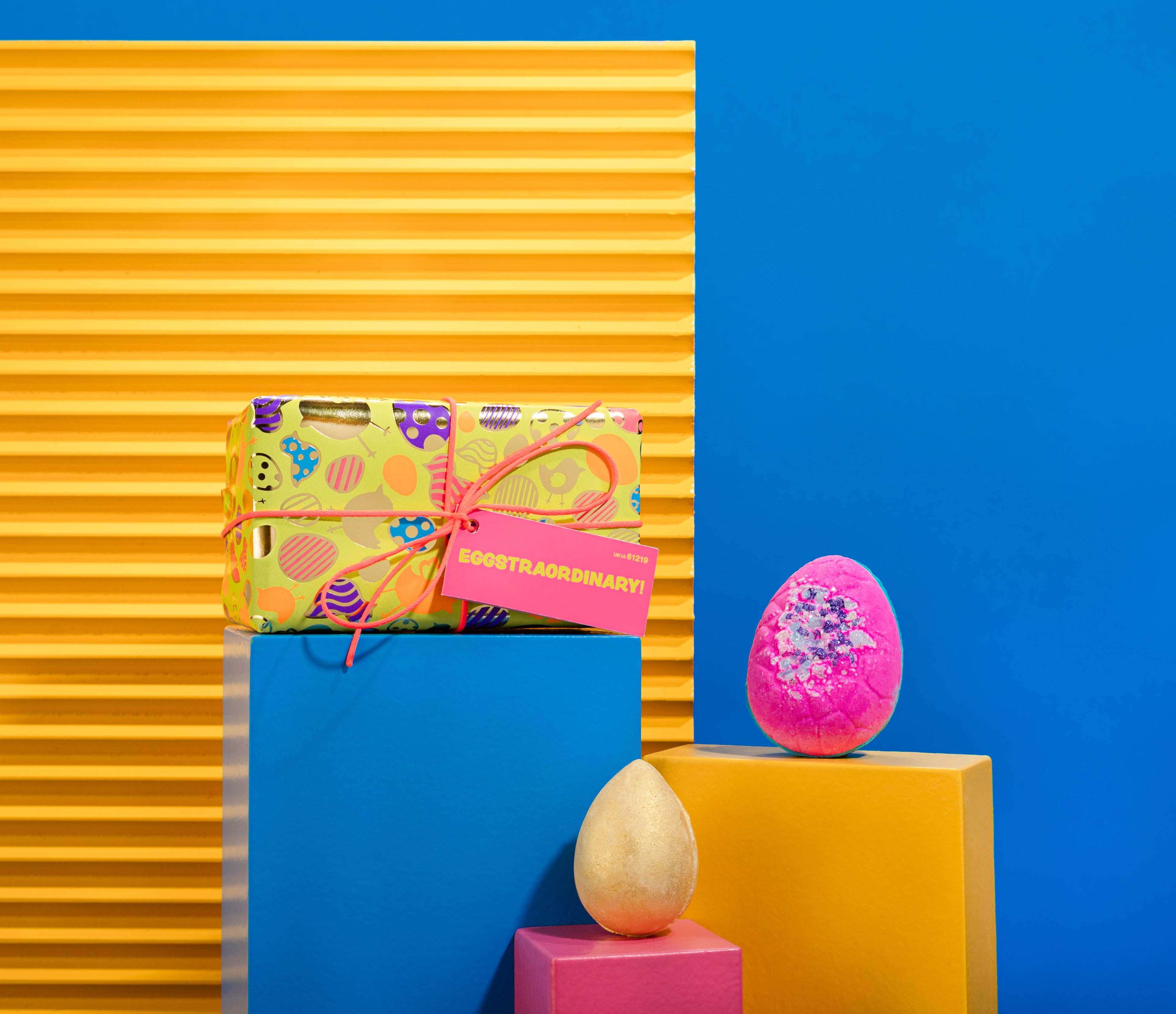 Eggstraordinary!, in front of a blue and yellow background, surrounded by its products on blue and yellow plinths.