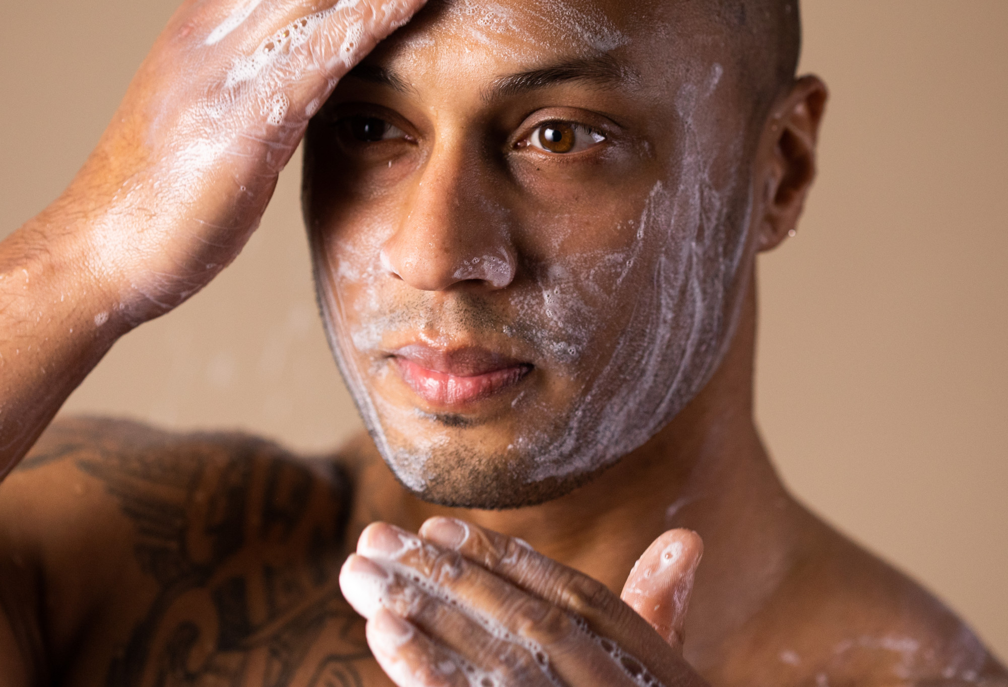 A bearded person's face is covered in whiteish soap suds, which are being rubbed into the skin at the forehead.