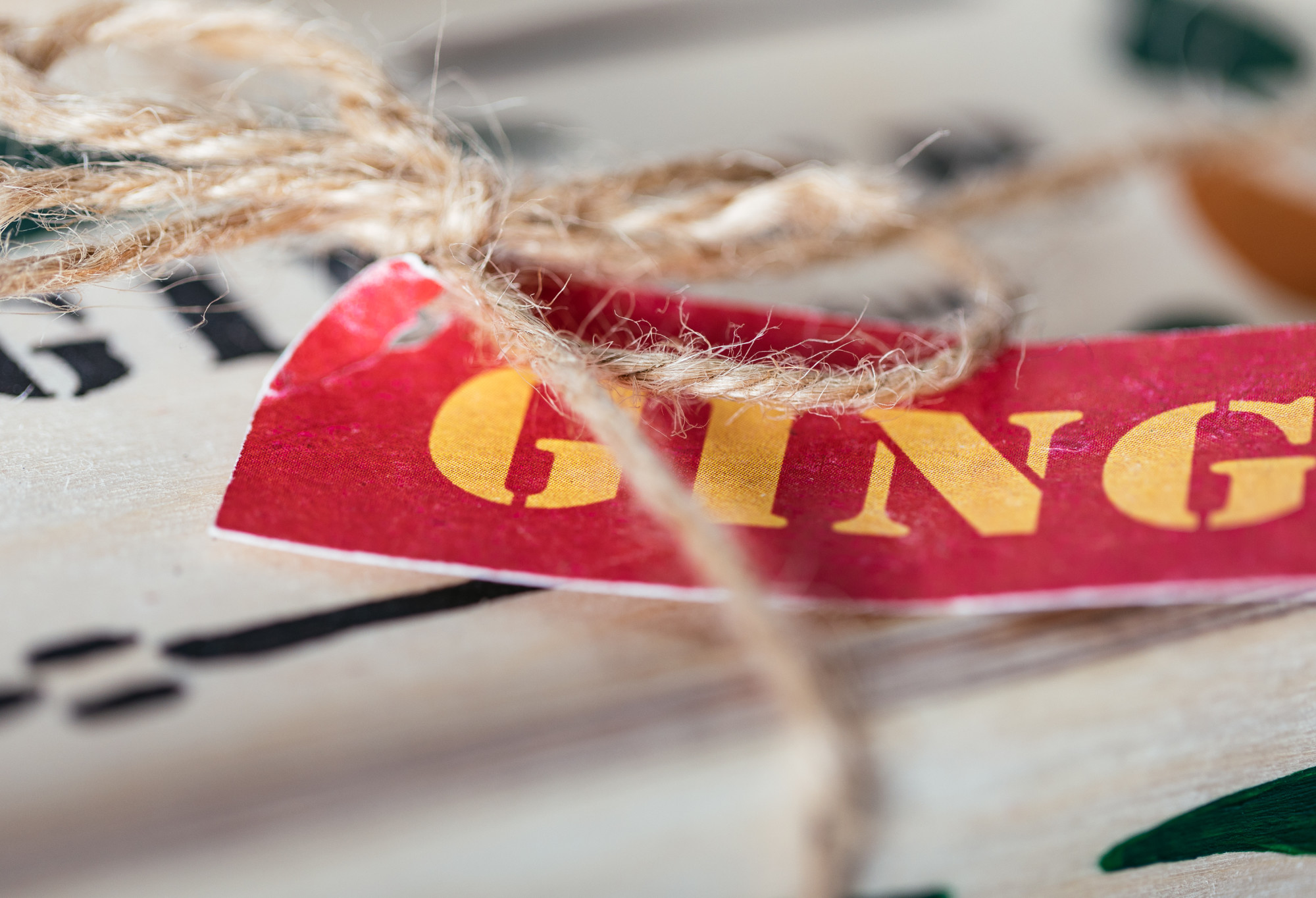 A close up of a red paper gift tag, with Ginger written on it in yellow writing, with a brown piece of string tied to it.
