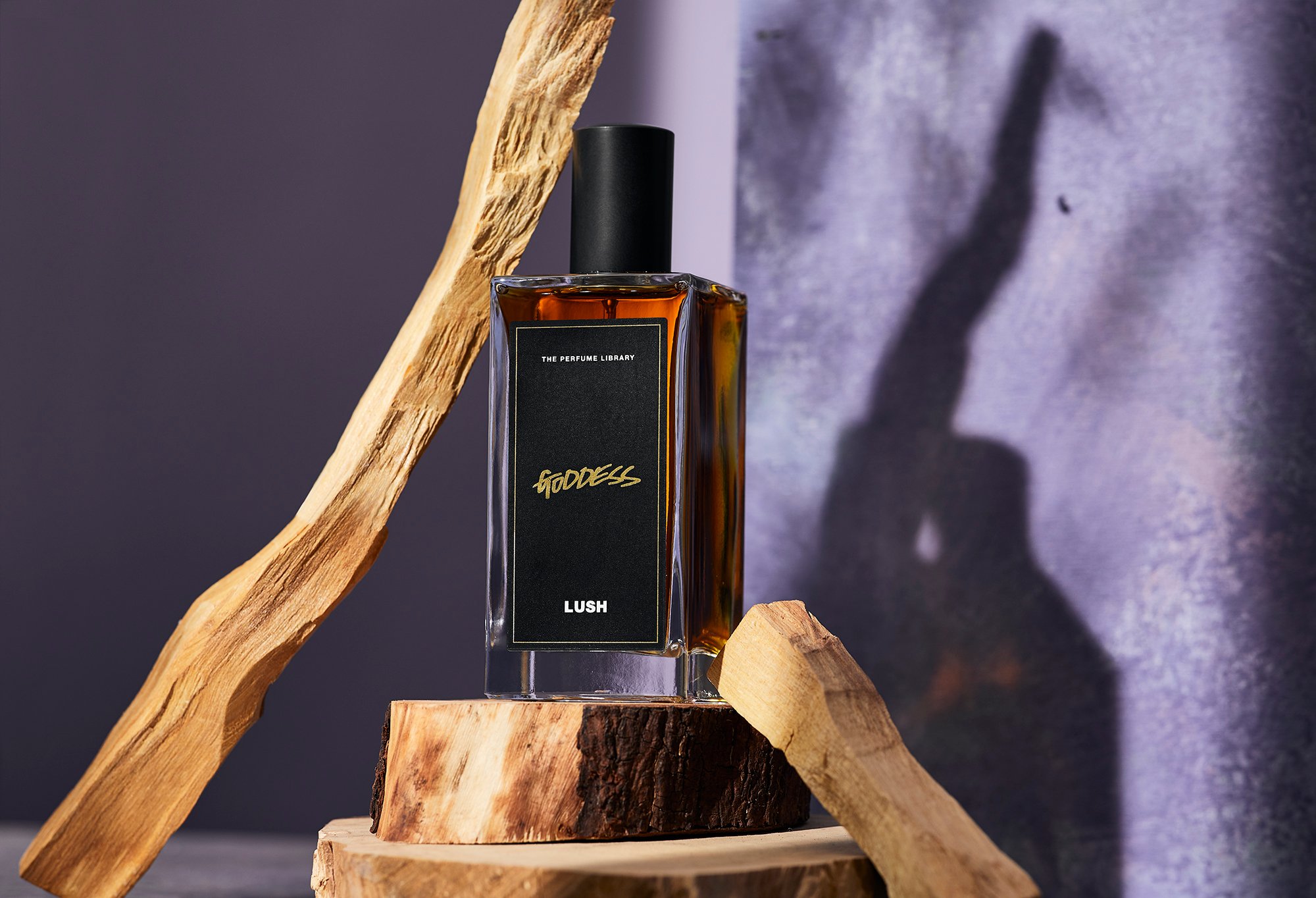 A dark amber coloured bottled perfume, Goddess, sits on top of a display of sandalwood, one of it's main ingredients.