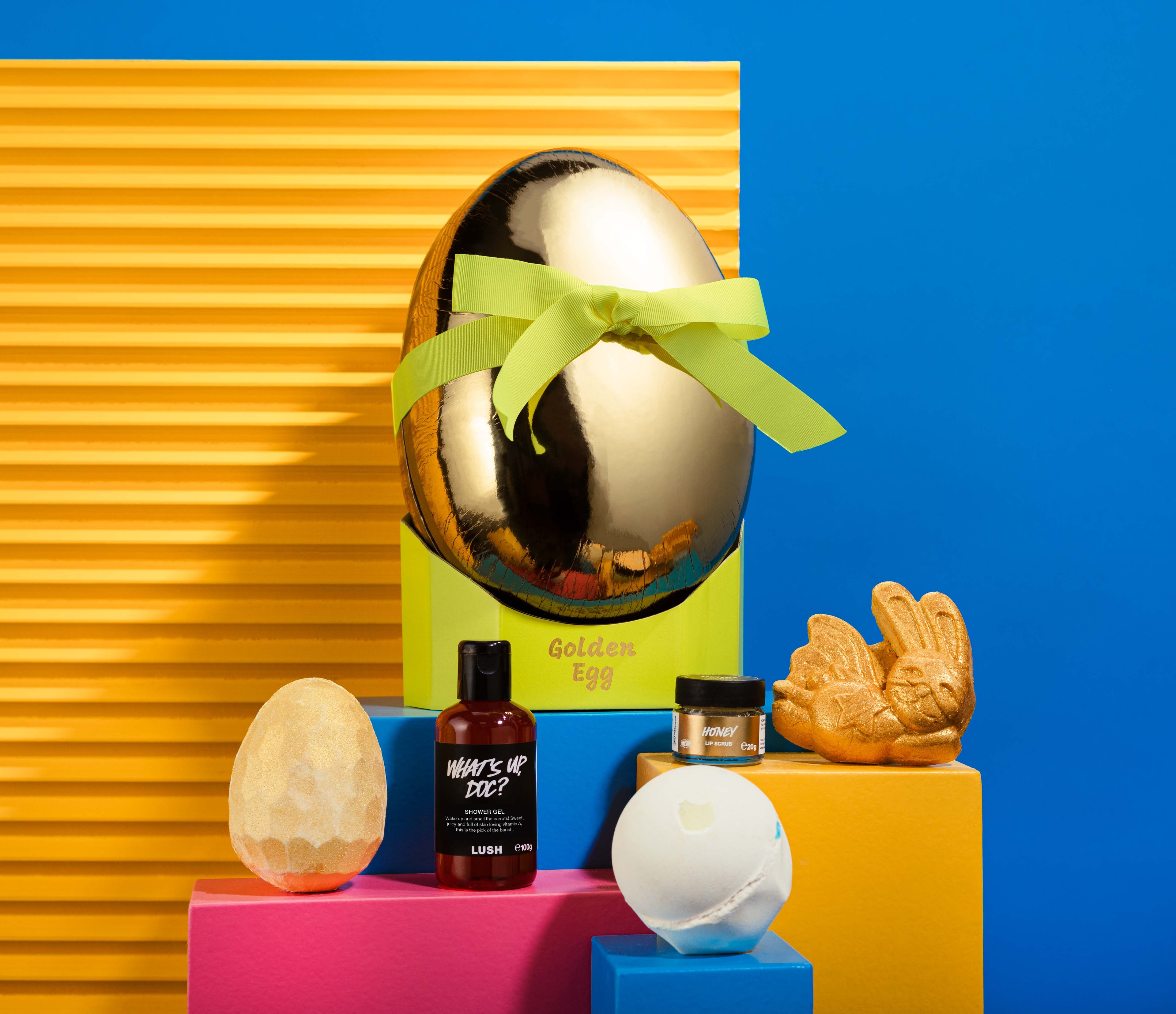 The gift in front of a blue and yellow background, surrounded by its products on blue, yellow and pink plinths. 