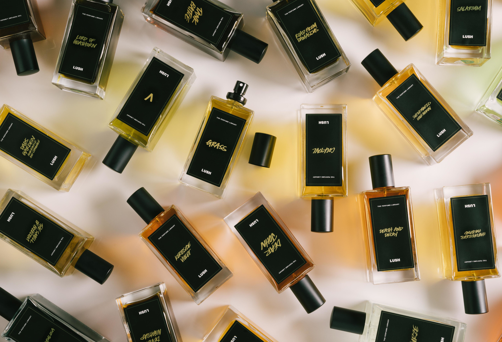 A number of black label perfume bottles are arranged randomly, with Grass in the centre, lid off, ready to spritz.