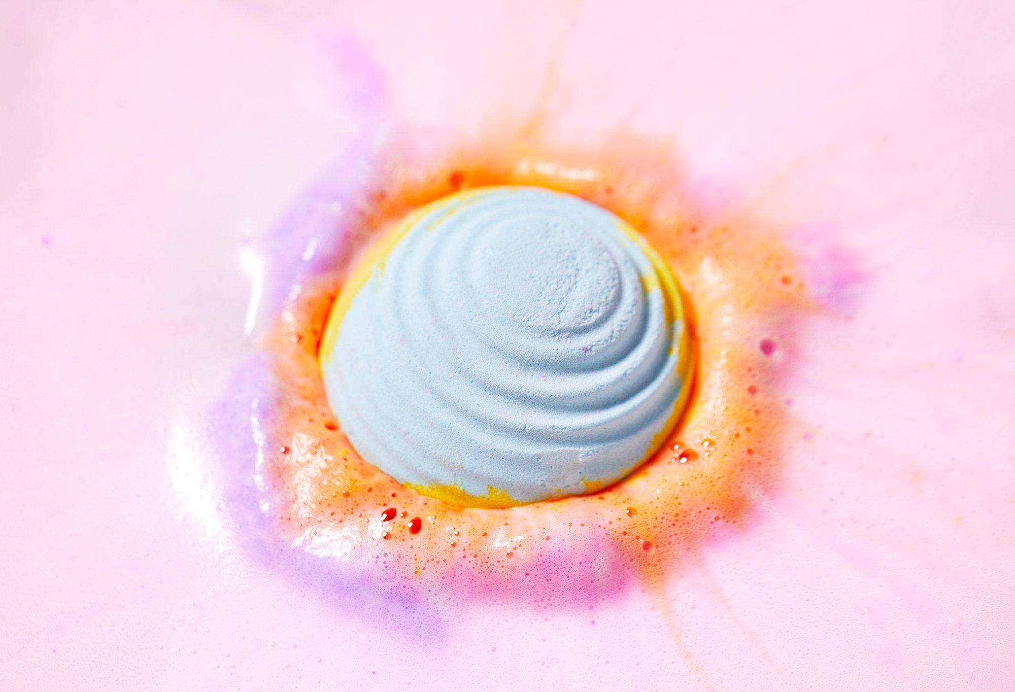 Groovy Bath bomb sits in the water surrounded by vibrant pinks, purples, oranges and blues for a funky fresh bath.