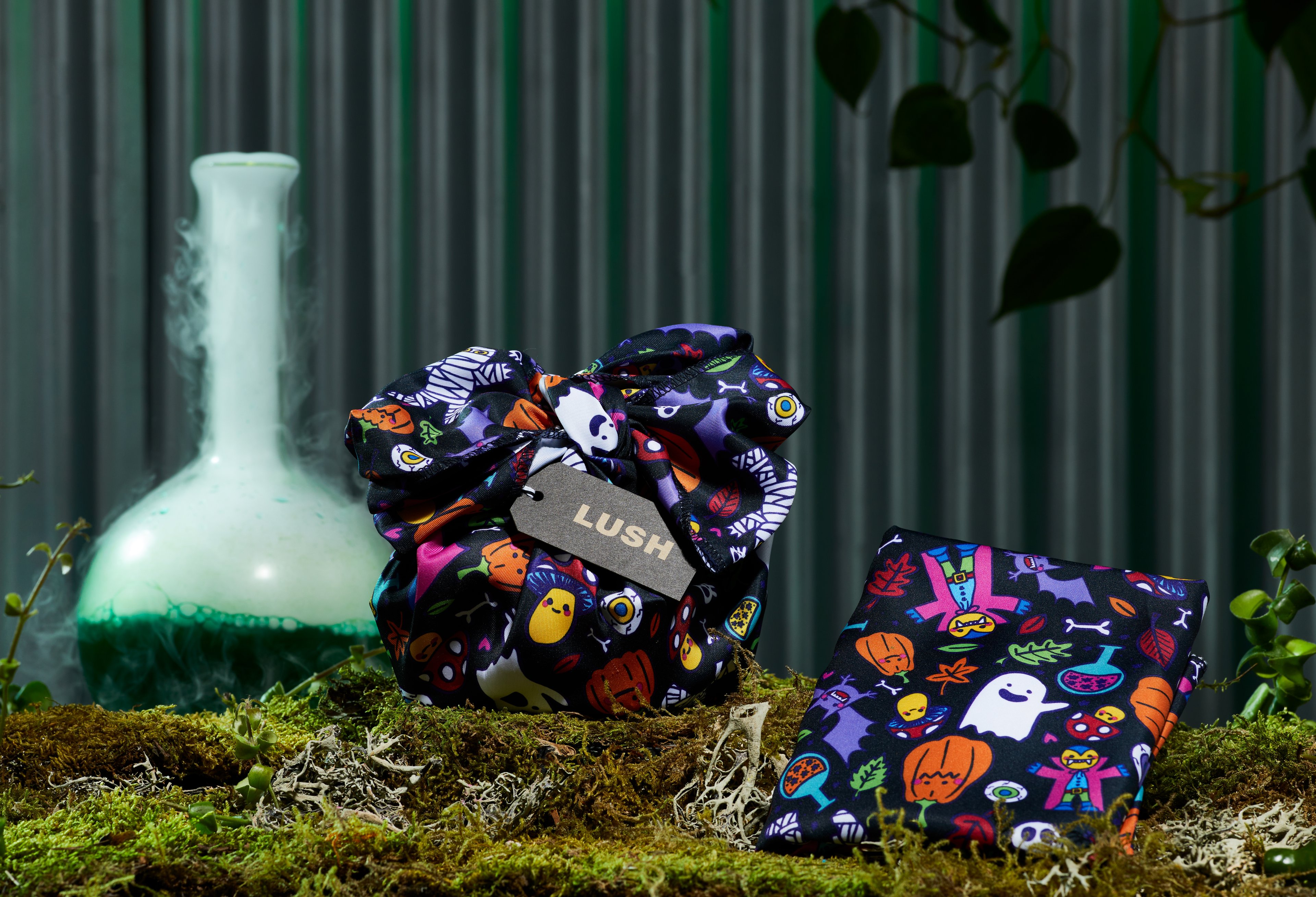 Happy Halloween Knot Wrap, displayed in two separate ways in front of a dark green background, on a bed of moss. 