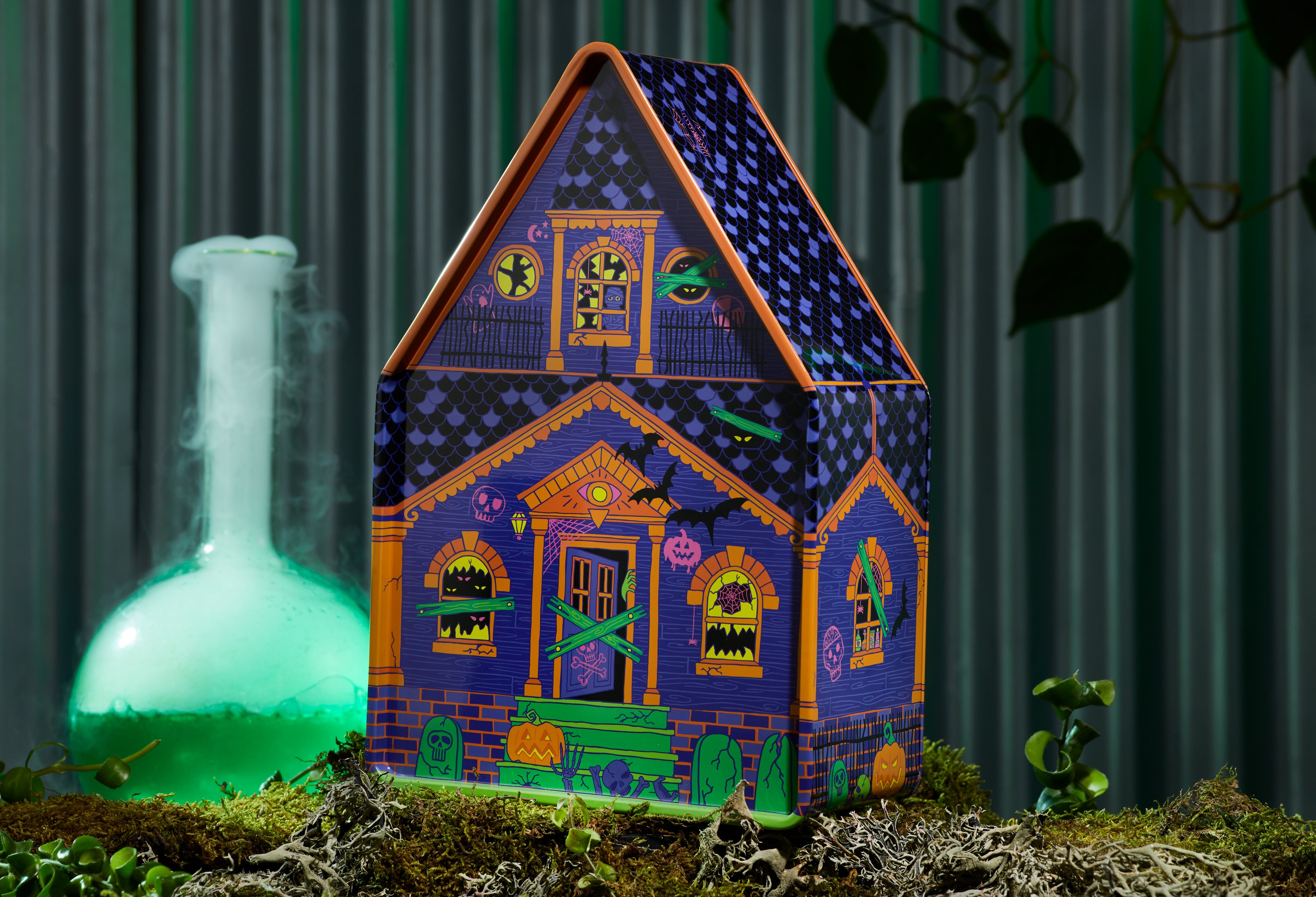 Haunted House Tin, in front of a dark green background, on a bed of moss. 